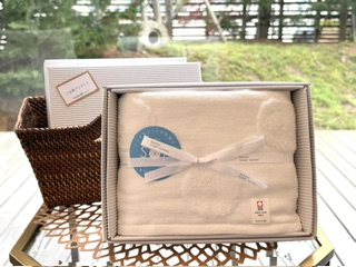 Gift box containing a folded beige towel tied with a white ribbon on a glass patio table outdoors.