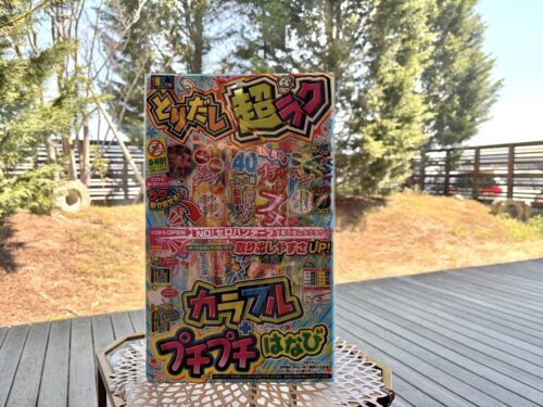 Colorful Japanese toy packaging on a stand outdoors, set on a metal lattice table with trees and a deck in the background.